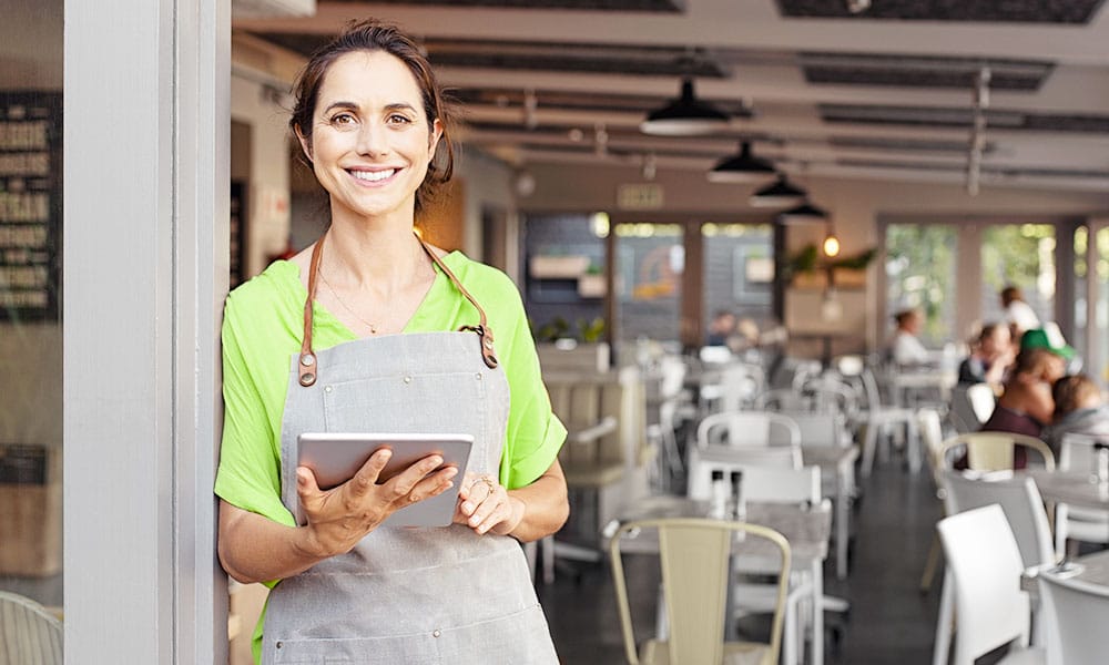 Female restaurant worker smiles at camera while holding iPad