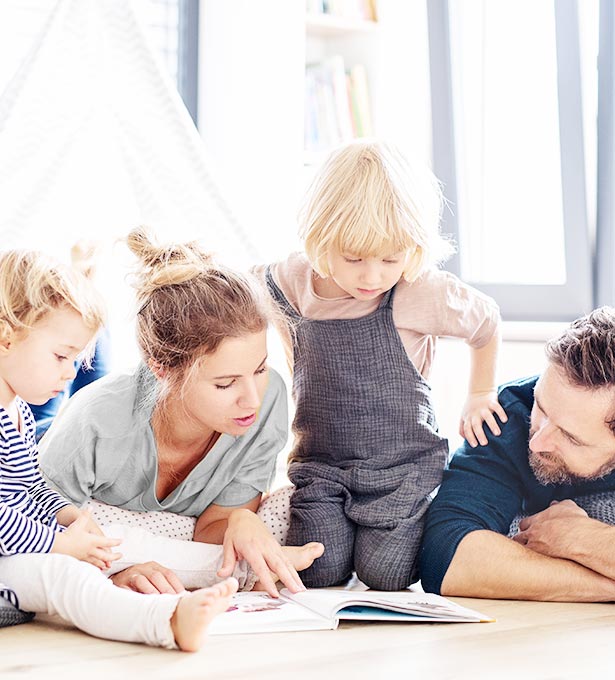 Couple and two toddlers reading a book together on house floor