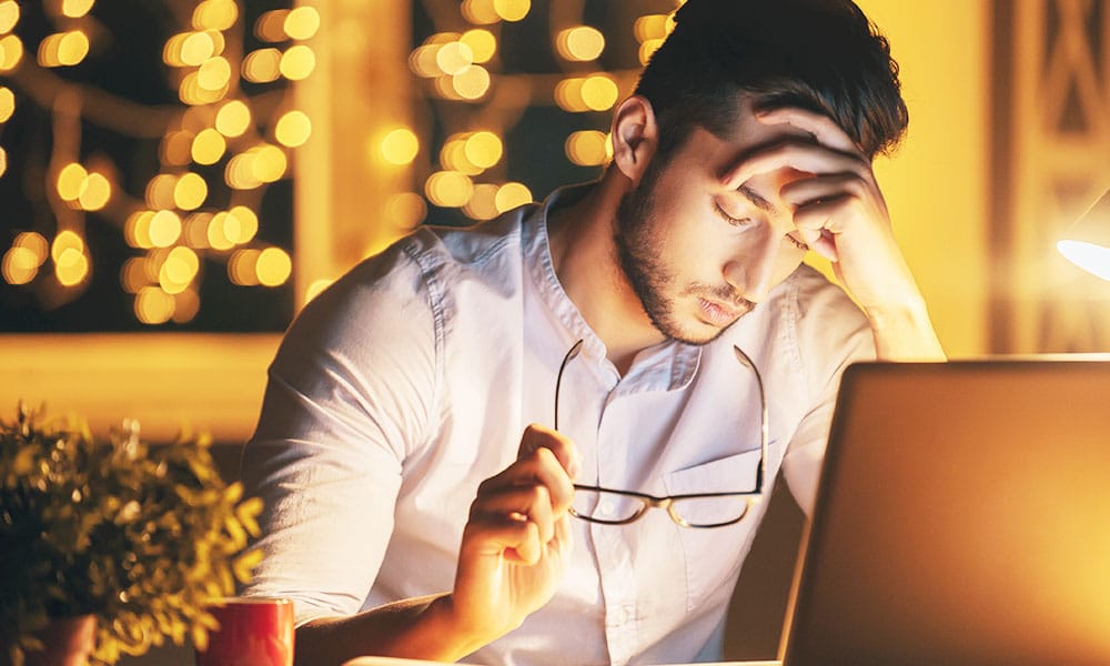 Millenial stressed out holding glasses late at night on computer