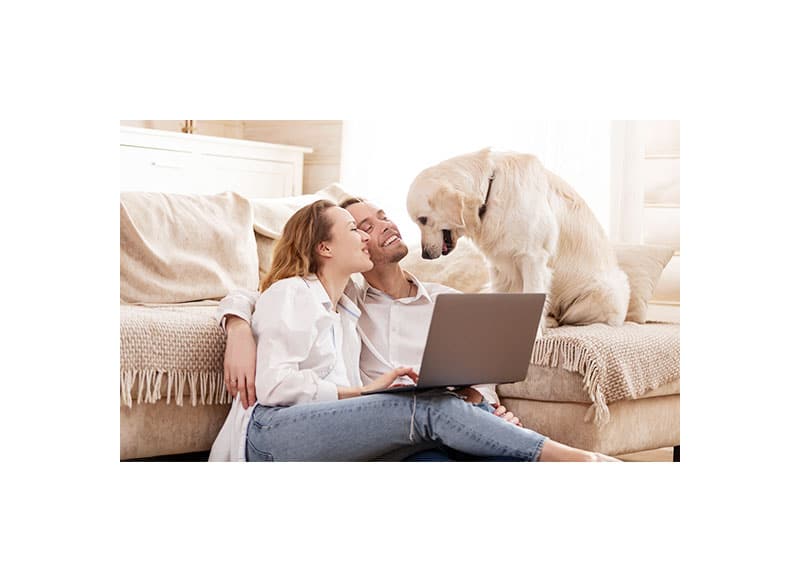 Young couple on computer laying against couch with dog