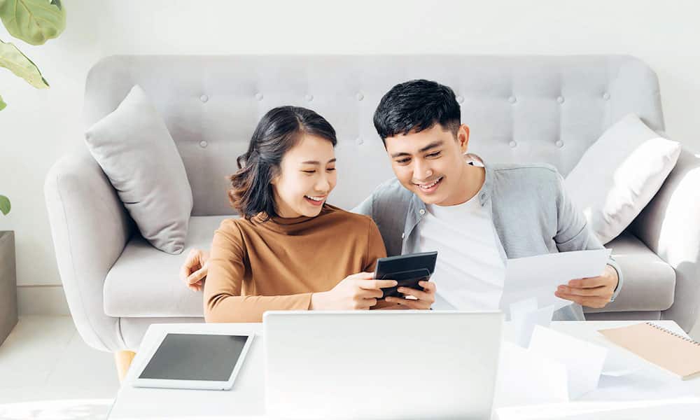 Young couple laying against grey couch calculating finances